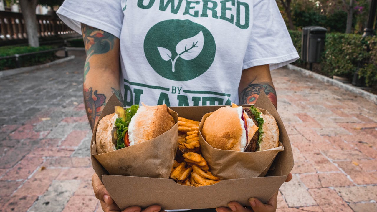 person holds box of vegan burgers and fries